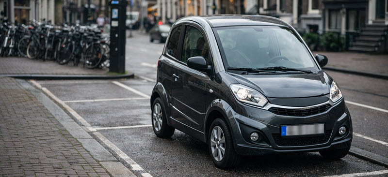 Elektrische microcar geparkeerd in de stad, passend bij regels rond parkeervergunningen.